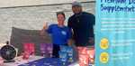 Two PupGrade team members smiling at an outdoor event booth with branded pet supplements, a prize wheel, and a promotional banner at Walmart’s Miami Pet Adoption Event.